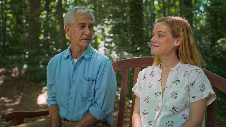 Older man and young woman sit on a bench in a park. The woman smiles at the man. Relationship. Generational.