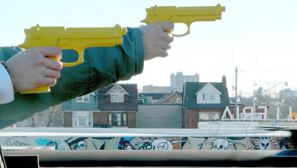 Hands holding yellow toy guns against a cityscape backdrop with graffiti. Gangsterism concept.
