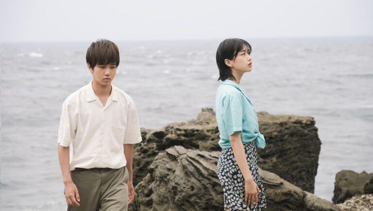 Two people on a rocky beach. Man in white shirt, woman in floral skirt. Ocean view. Coastal scene.