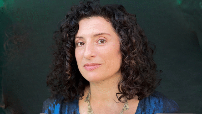 Headshot of Loktev, a woman with curly dark hair. Portrait against a dark background.