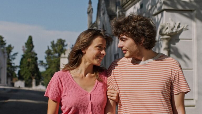 Smiling couple walking together outdoors. Woman in pink, man in striped shirt. Happy relationship.