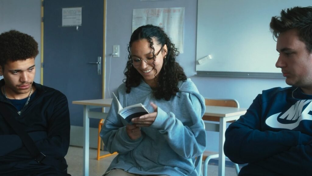 Laguna film review: Teenagers in a classroom. A girl reads a book, smiling. Šarūnas Bartas film, Venice '25.