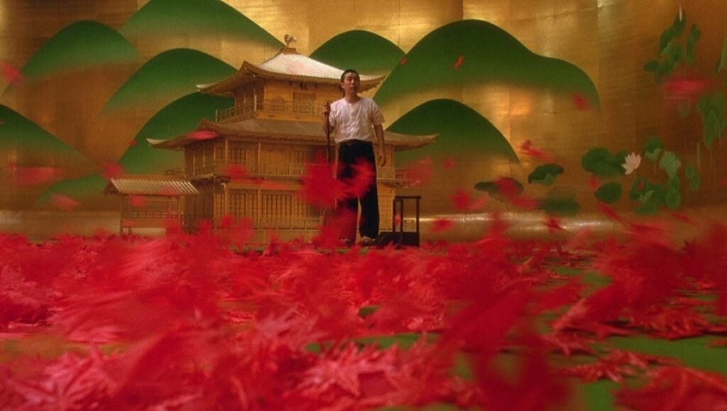 Mishima film scene. Man stands before golden temple, red leaves scattered. Japanese cinema.