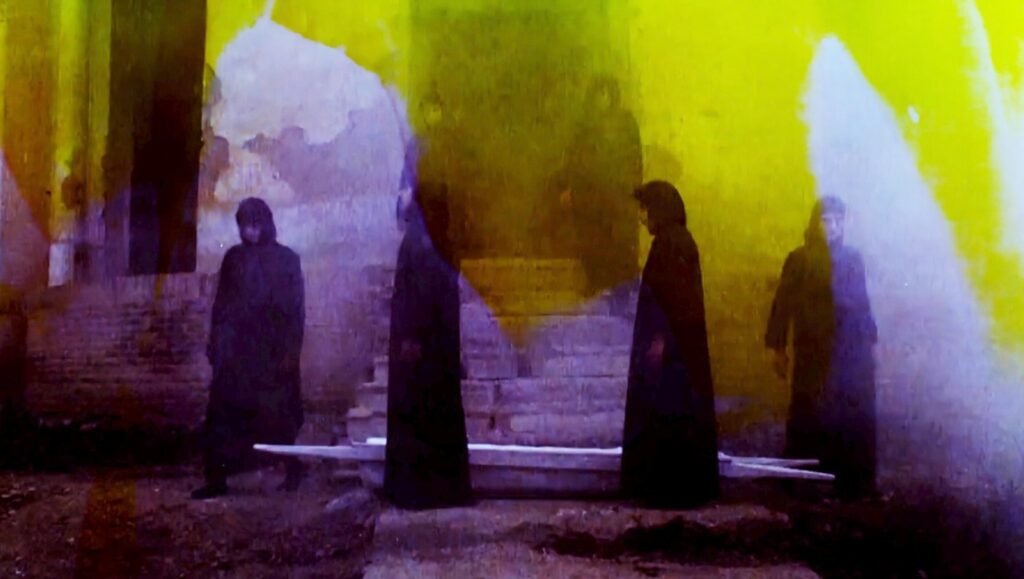Night Flowers film still. Four figures in dark robes stand in a surreal, dreamlike setting. Wavelengths 2: Into the Blue, TIFF '25 review.