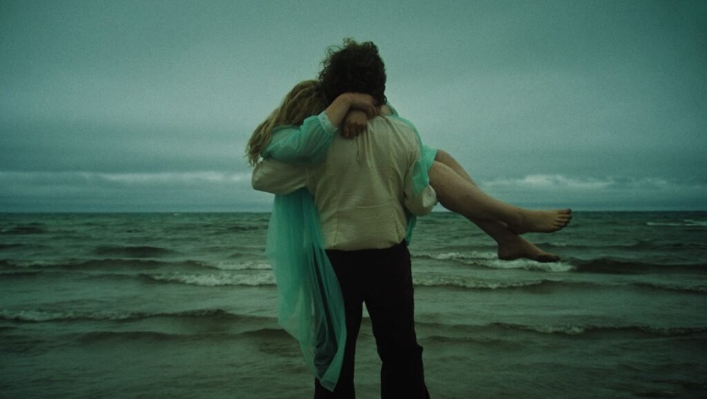 Romantic beach scene: Man carries woman in his arms by the ocean. Moody sky. Couple embracing.