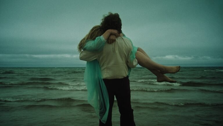Romantic beach scene: Man carries woman in his arms by the ocean. Moody sky. Couple embracing.