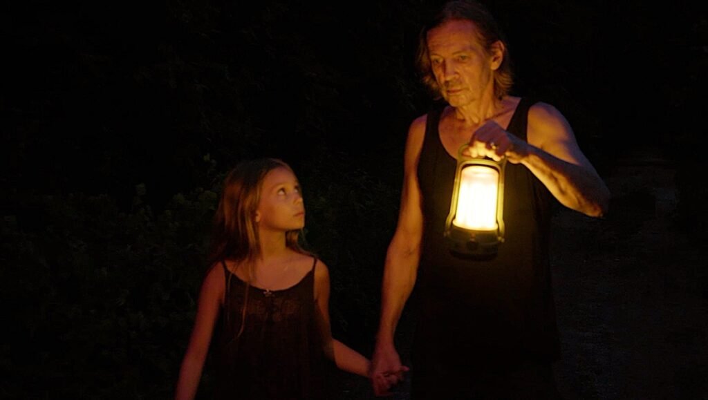 Laguna film review: A man and a girl hold hands in the dark, lit by a lantern. Šarūnas Bartas film still.