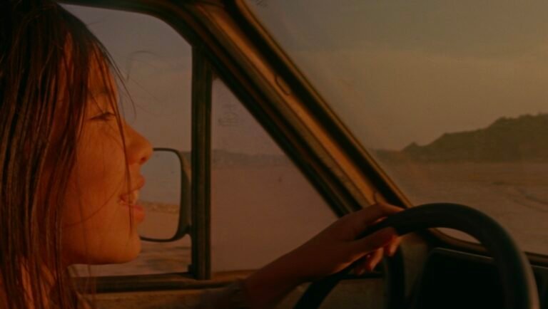 Still from *Mares Nest* at TIFF 2025. Woman driving a car, looking out at a desert landscape.