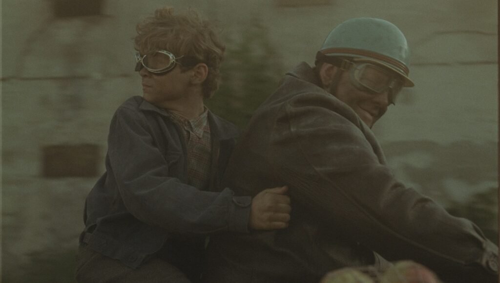Still from 100 Sunset: Two figures, one in goggles, the other in a helmet, ride together. Kunsang Kyirong TIFF '25 review.
