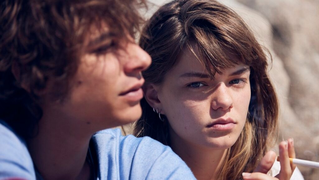 Film still from Romería at NYFF63: Two young people, one smoking, gaze intently. Drama, youth, cinema.