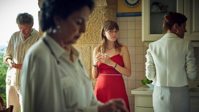 Romería film still: Family gathering in kitchen. Woman in red dress. Carla Simón, NYFF '25 review.