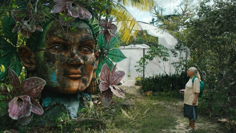 Woman views large face sculpture in lush garden. Art and nature blend in this unique outdoor space.