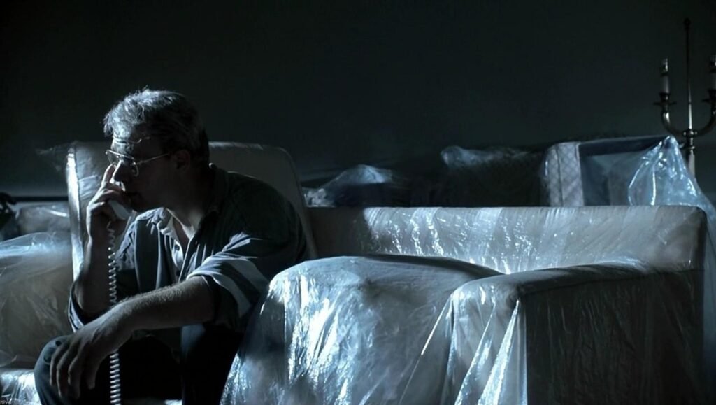 The Insider film essay image: Man on phone sitting on plastic-covered furniture. Dark, tense scene.