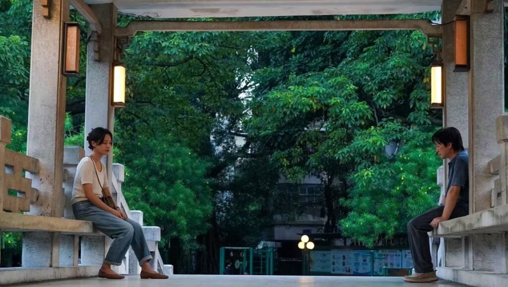 The Sun Rises On Us All still: Two people sit apart in a park pavilion. TIFF 2025 film.