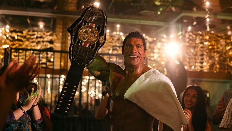 Dwayne Johnson as Mark Kerr in The Smashing Machine movie. Wrestler with championship belt and towel. A24 film review.