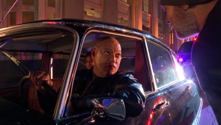 Mike Figgis' Megadoc review: Shaven-headed man in car with another man leaning in.