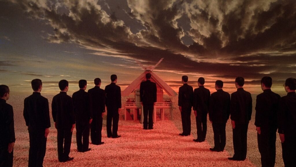 Where the Filmmaker Pours Himself In: Paul Schrader’s Mishima: A Life in Four Chapters Mishima: Men in suits face a Japanese shrine under a dramatic sky. Art film scene.
