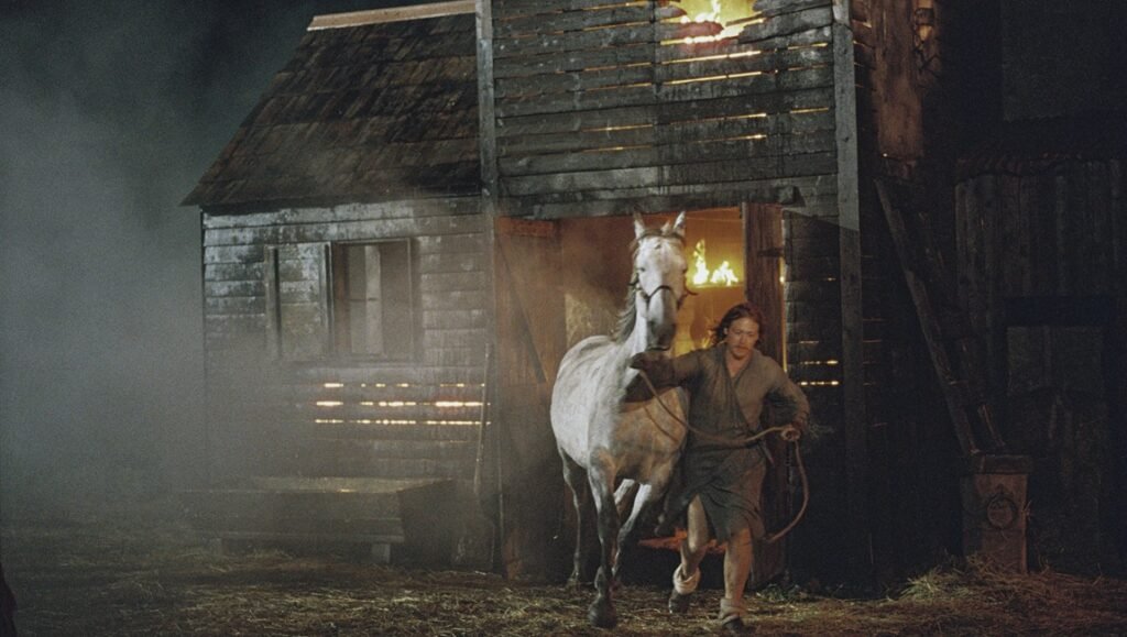 August 2025 — Reviews Roundup Harvest movie scene: Man leads white horse from burning barn. August 2025 film review.
