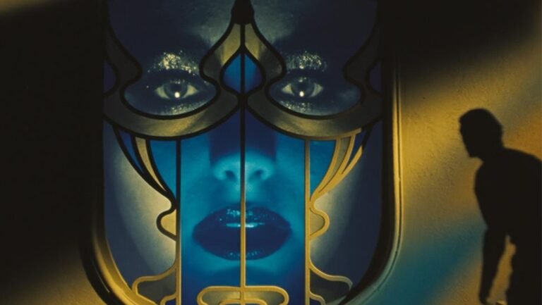 Orfeo film still from Venice Film Festival 2025 dispatch. Blue-toned face behind ornate frame, shadow of a man.