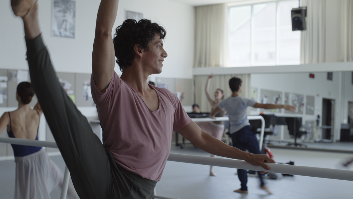 Ballet dancer stretches at the barre in a dance studio. Ballet class with other dancers. Dance training.