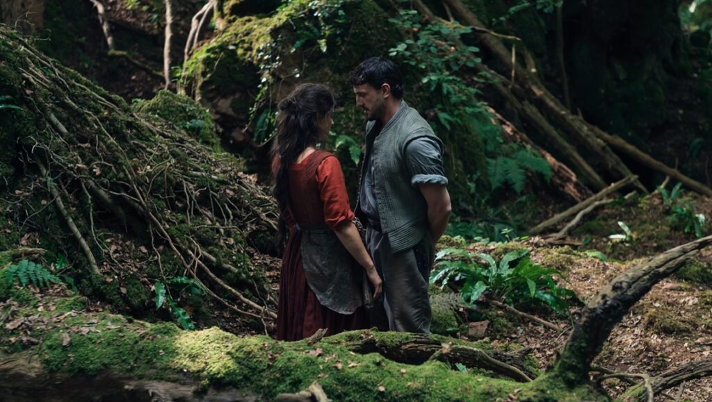 Hamnet movie scene: Couple in period clothing stand in a lush forest, looking at each other.