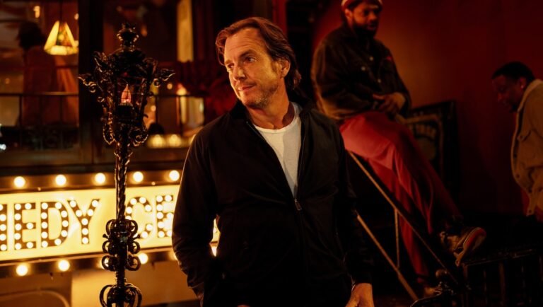 NYFF 2025 film still: Man in black jacket in front of Comedy sign. Is This Thing On? film image.