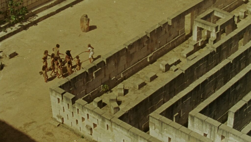 Ben Rivers' Mare's Nest film still: Children playing near a stone labyrinth, evoking imagination and ancient ruins.
