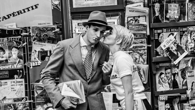 London Film Festival: Nouvelle Vague film still. Couple kissing by a magazine stand. Black and white.