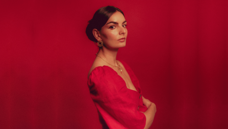 Between the Production and Real Life: Paula González-Nasser on The Scout Paula Gonzalez Nasser portrait. Woman with jewelry, red dress, and red background. Jamie Rice photographer.