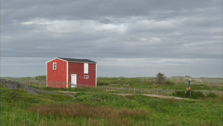 Still from Sharon Lockhart's Windward featuring a red house and person on stilts.