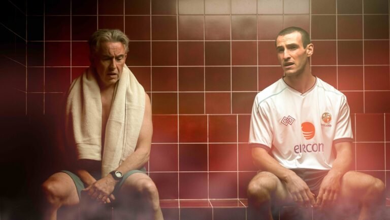 Two soccer players in a locker room. One with a towel, the other in an Ireland jersey.