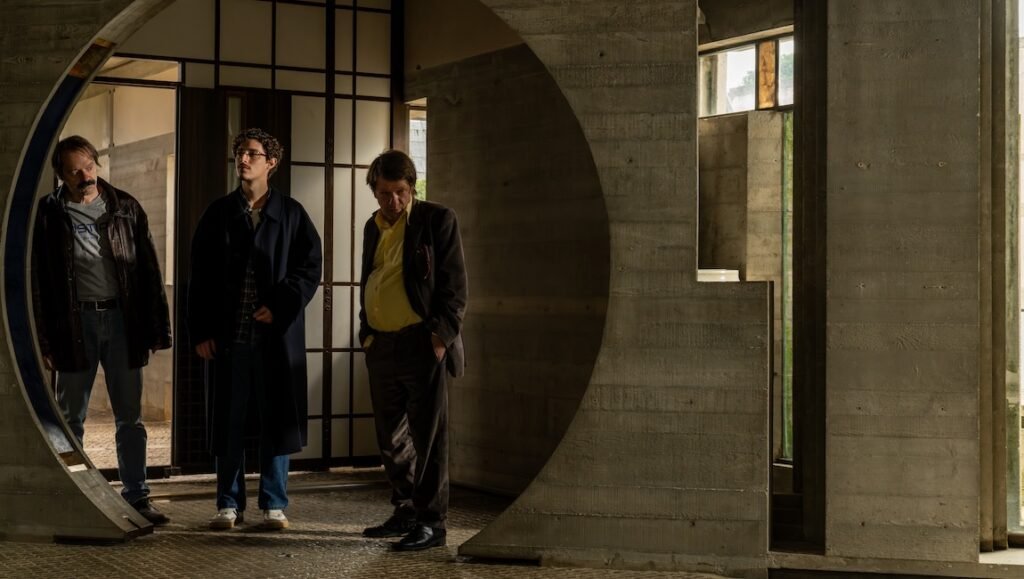 The Last One for the Road film still. Three men stand in a modern building. NYFF '25 review.