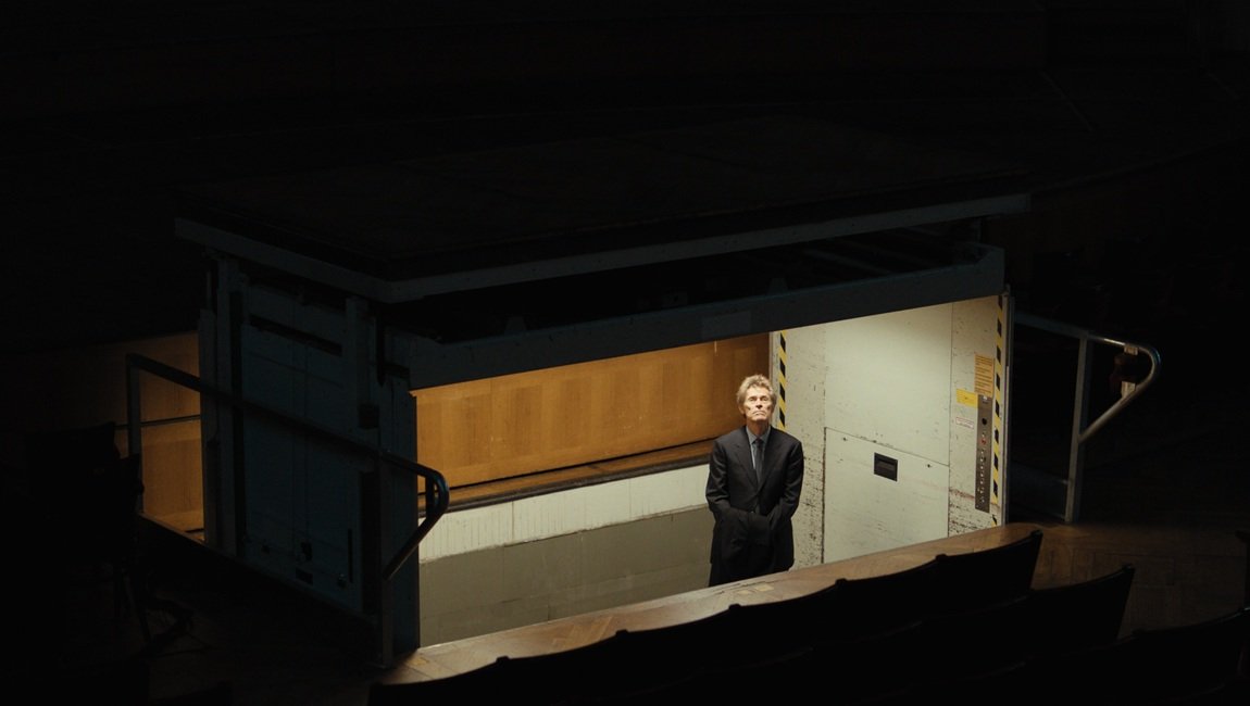 Theater Souffleur: Man in a suit stands in a box at the opera, ready to prompt actors. Stage production.