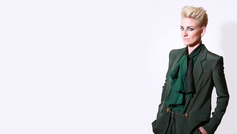 All Queens, No Divas: Tina Romero on Queens of the Dead Tina Romero headshot. Woman with short blonde hair wearing green suit.