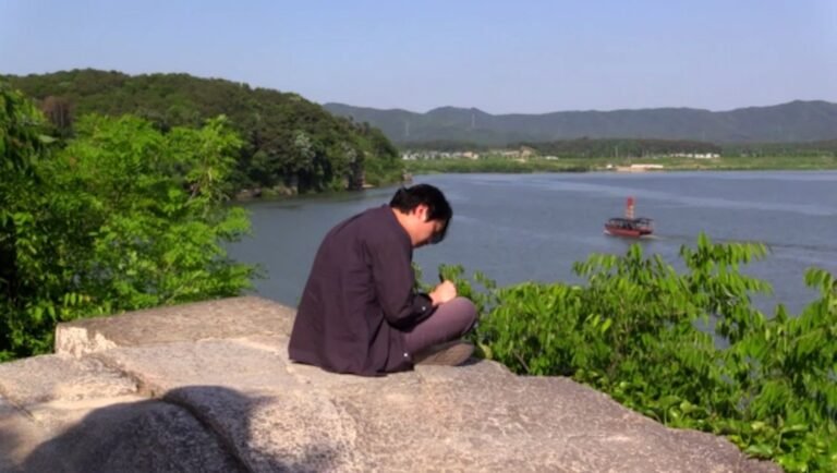 Hong Sang-soo film still. Man contemplates nature by a river. What Does That Nature Say To You? NYFF '25 review.