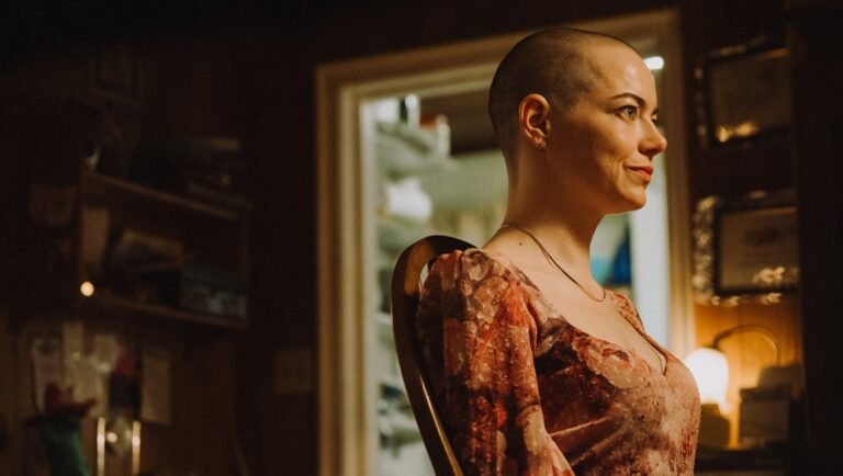 Profile view of a woman with a shaved head wearing a floral dress.