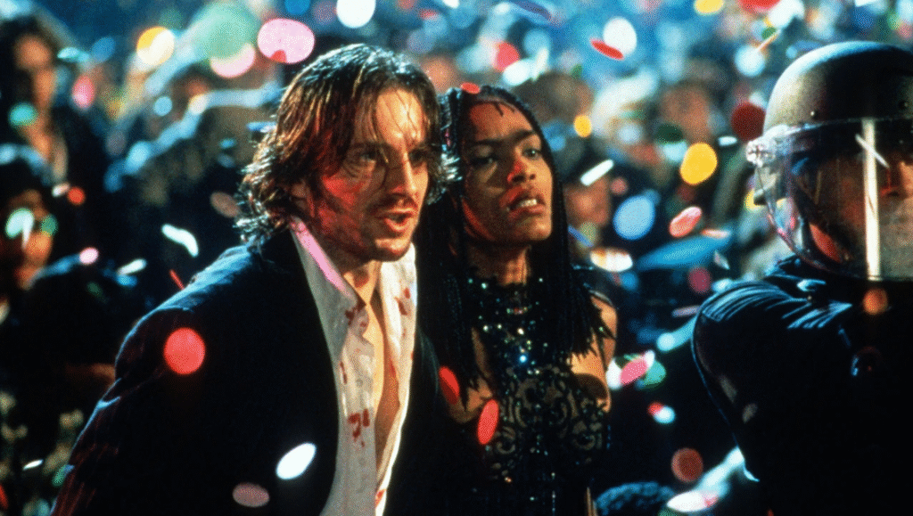 Strange Days movie scene with Ralph Fiennes, Angela Bassett, and a riot police officer amid confetti.