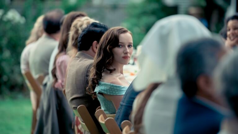 Phoebe Dynevor in Anniversary movie. Woman at long table, looking back. Lionsgate film.