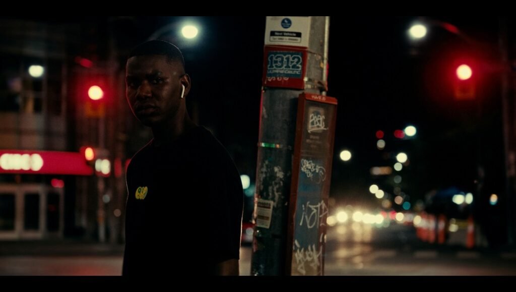 Reza Dahya portrait at night. City street with lights and traffic. Man with earbuds. A Baby Step Into Vulnerability.