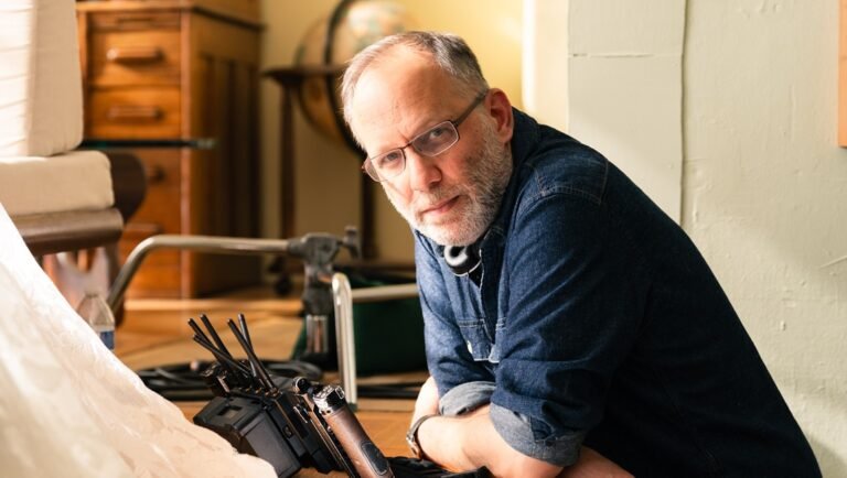 Director Ira Sachs on set. Sachs wears glasses and a denim shirt, with film equipment nearby.