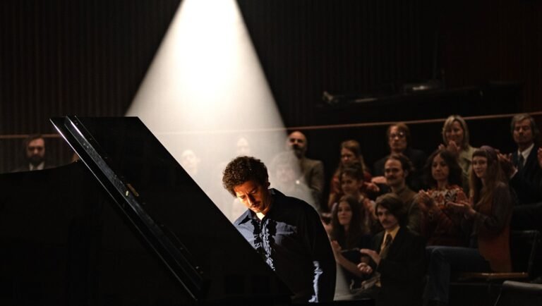 Jan Komasa's Anniversary review image. Pianist performs for an audience under a spotlight. Zeitgeist.