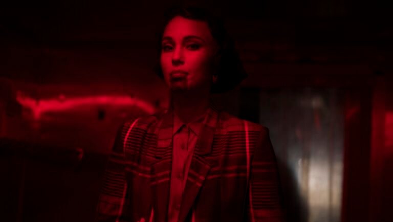BLKNWS review image: Portrait of a woman in a plaid blazer, bathed in red light, for Kahlil Joseph's art film.