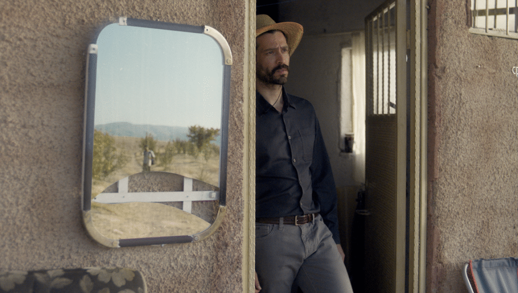 Alireza Khatami in The Things You Kill. Still from the film featuring a man in a doorway and a mirror reflecting a landscape.