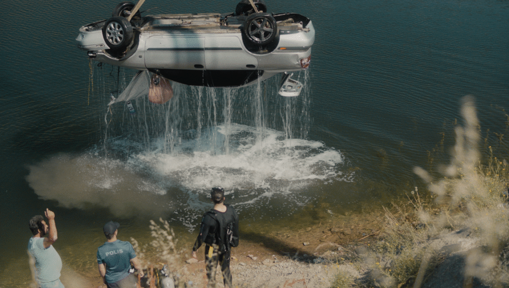 The Things You Kill film still: Car being lifted from water, police watching.