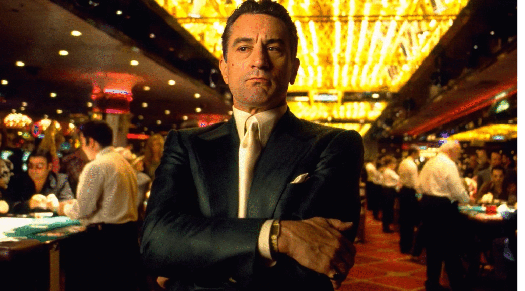 Robert De Niro in Casino movie, arms crossed in a vibrant, crowded Las Vegas casino. Gambling and vintage style.