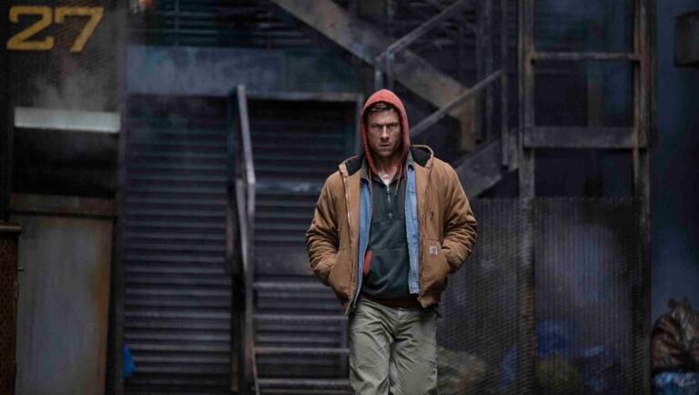 Still from The Running Man review. Man in hoodie and jacket walks in urban setting.