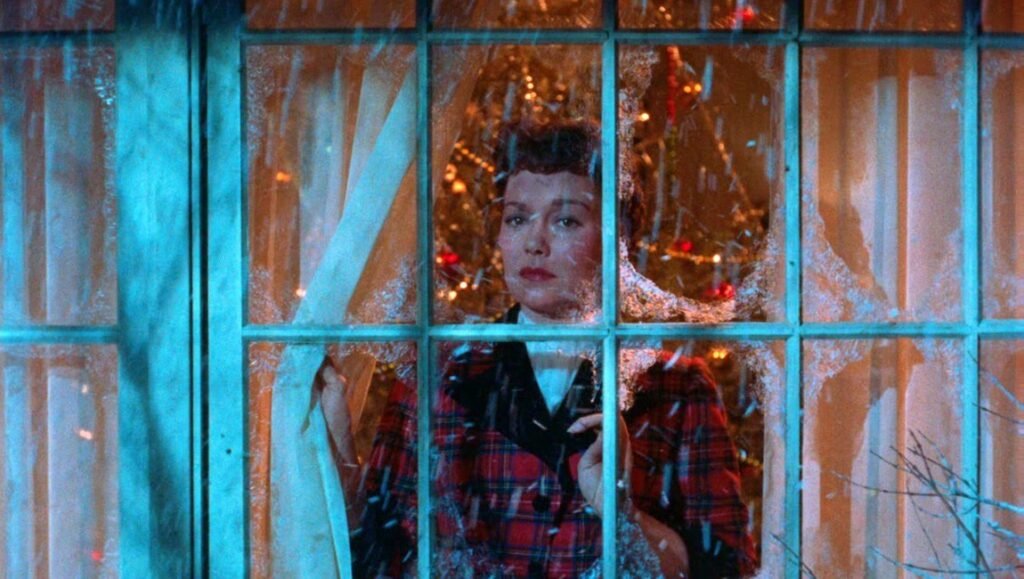 All That Heaven Allows image: Woman gazes through a frost-covered window at Christmas lights, reflecting on life.