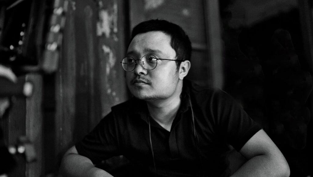 The Pursuit of Autonomy & Freedom: A Conversation with Bi Gan on Resurrection Black and white headshot of Bi-Gan, a person with glasses looking thoughtfully to the side. Portrait, artistic.