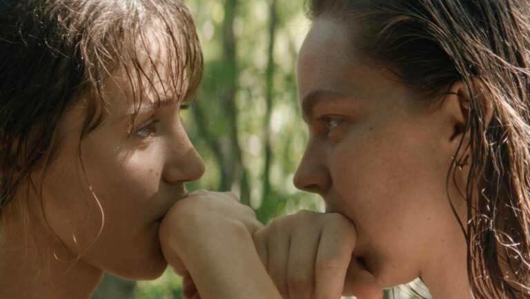 Little Trouble Girls review: Two young women share a tender, intimate moment in this film still, holding hands to their mouths.