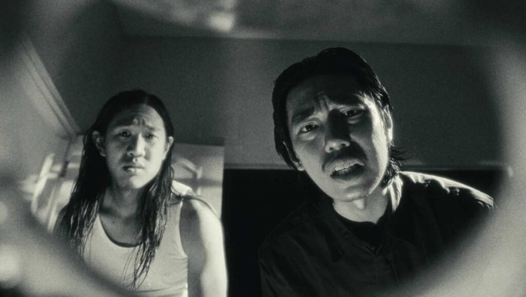 Manhole film still from Singapore International Film Festival 2025, featuring two worried men in a black and white scene.